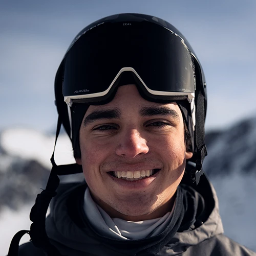 Person wearing a black crewneck shirt with a small logo, standing against a plain light gray background.
