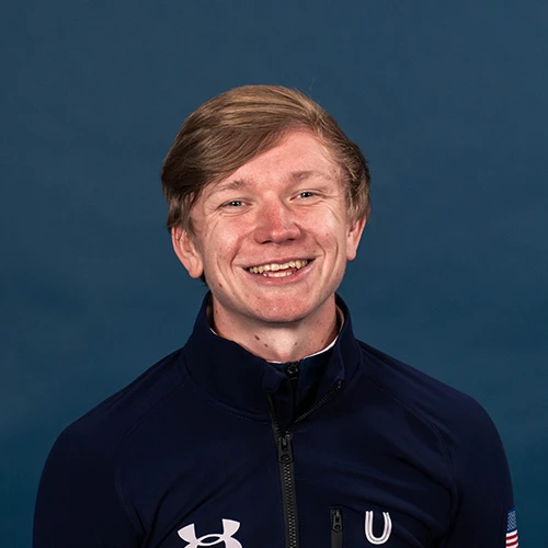 Person wearing a black crewneck shirt with a small logo, standing against a plain light gray background.