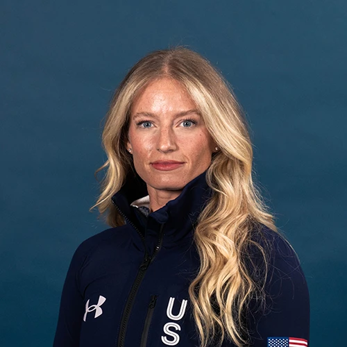 Person wearing a black crewneck shirt with a small logo, standing against a plain light gray background.