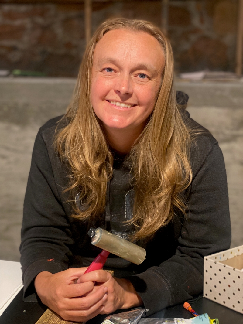The artist, smiling in a dark grey hoodie and holding a roller used to make woodcut pressings.