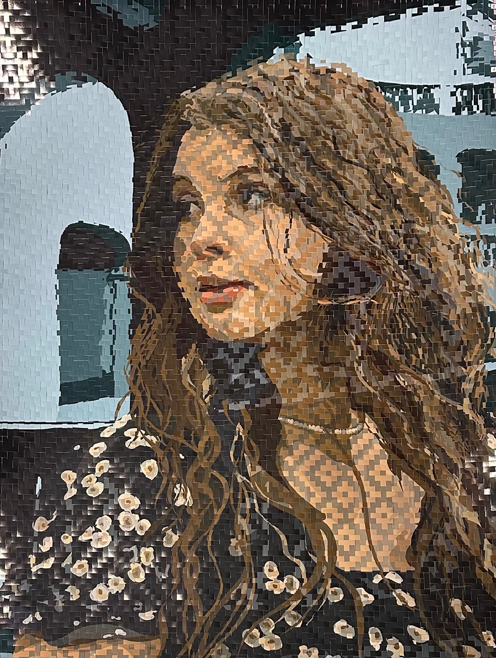 Photograph. A woman with long brown hair in a dark blouse with a floral print. She's looking back, over her right shoulder, face in three-quarter profile, and the background suggests buildings seen through car or train windows. The picture is woven together of flat strips of paper, and the artist has created patterns of concentric diamonds on the woman's skin.