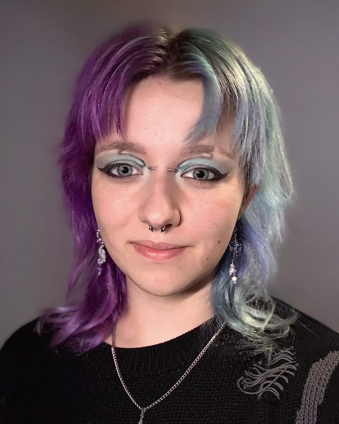 A close headshot of the artist with pronounced cat-eye makeup and hair that’s half purple and half blue.
